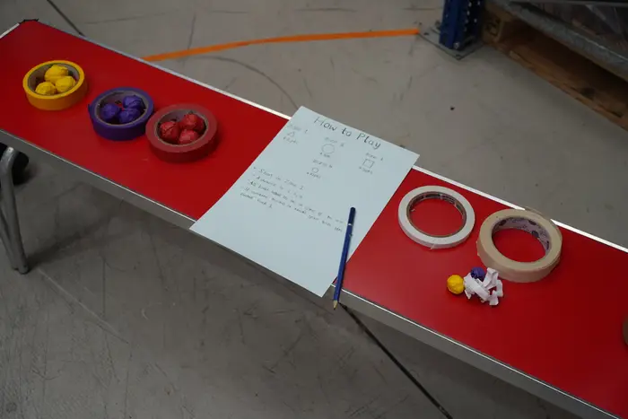 A handwritten How To Play sheet on a red table with game pieces