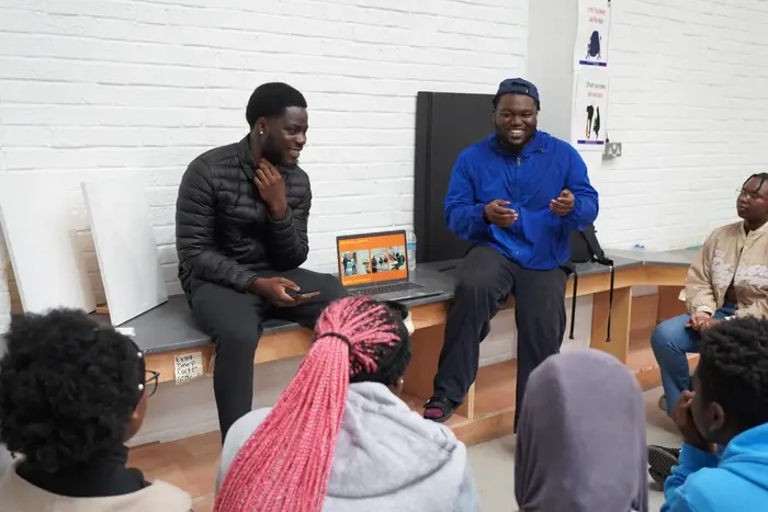 Two mentors talking with a group of young people in a workshop space